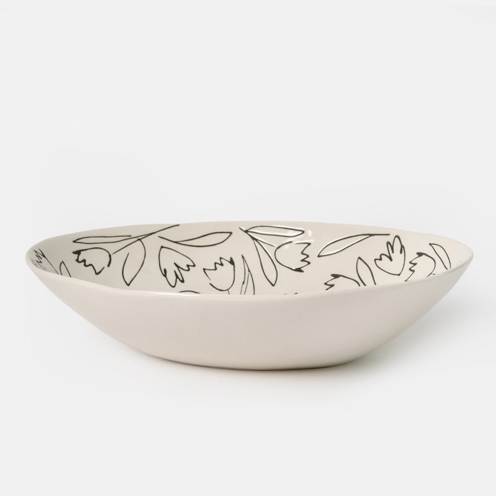 An oval ceramic bowl in a warm off-white or cream color, decorated with a delicate black hand-drawn floral and leaf pattern inside, shown on a seamless light gray background.