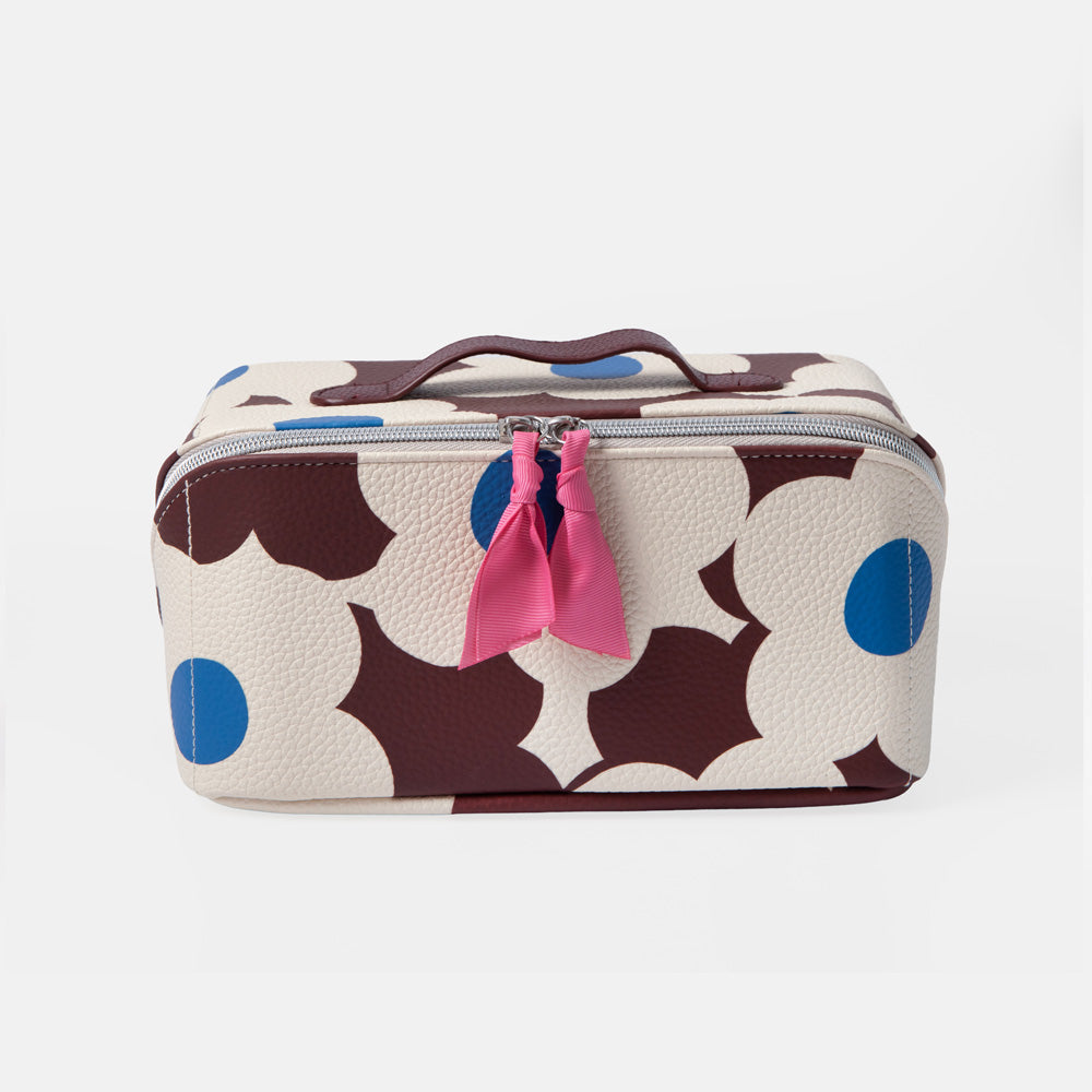 A rectangular zippered cosmetic bag with a cream background and a bold dark brown and blue floral pattern, featuring a pink ribbon tassel on the zipper.