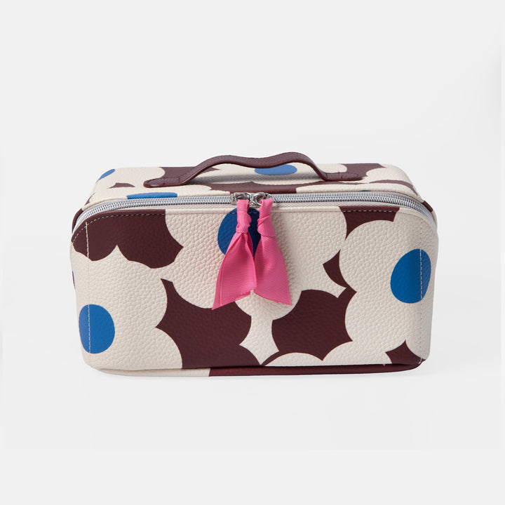 A rectangular zippered cosmetic bag with a cream background and a bold dark brown and blue floral pattern, featuring a pink ribbon tassel on the zipper.
