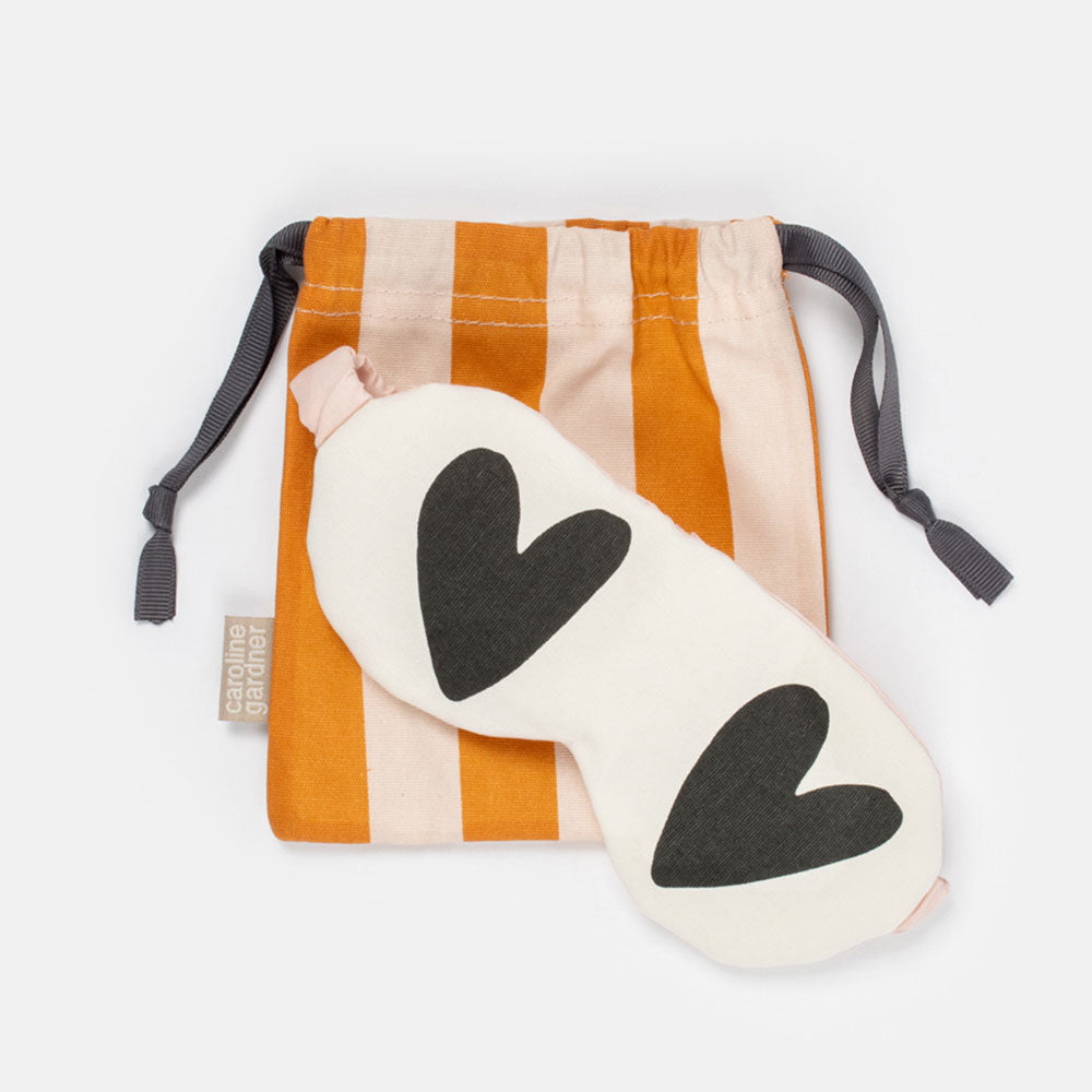 white and black hearts eye mask in a pink and orange striped drawstring cotton bag