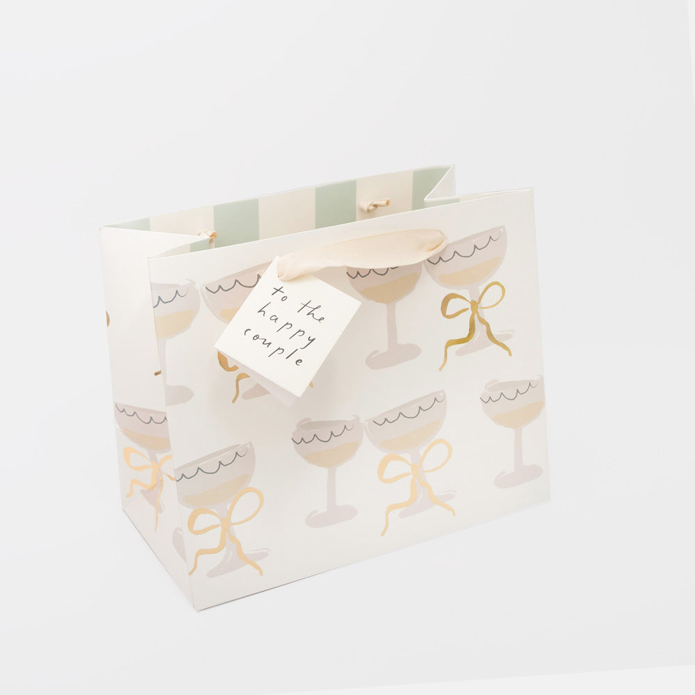 large wedding gift bag featuring a design of champagne glasses and a gift tag with the word 'to the happy couple' 