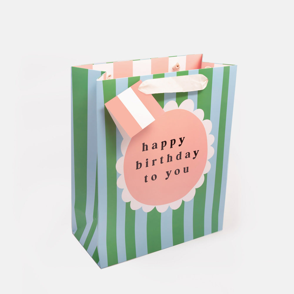 large gift bag in green and blue stripe design with pink flower in the middle with the wording 'happy birthday to you' 