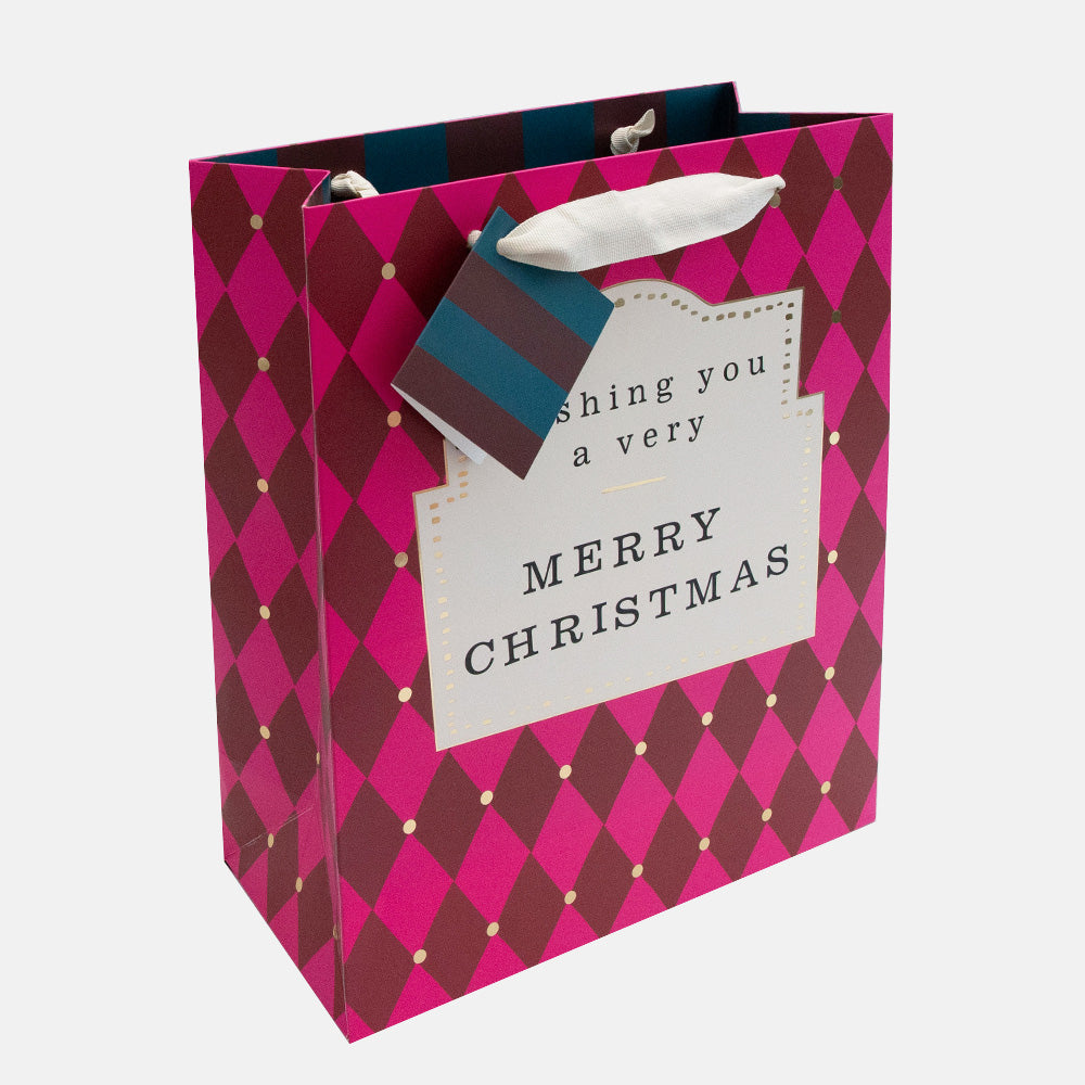 a Christmas gift bag in a pink & burgundy harlequin diamond design with large front label with 'wishing you a very Merry Christmas' text, and contrast striped gift tag. 