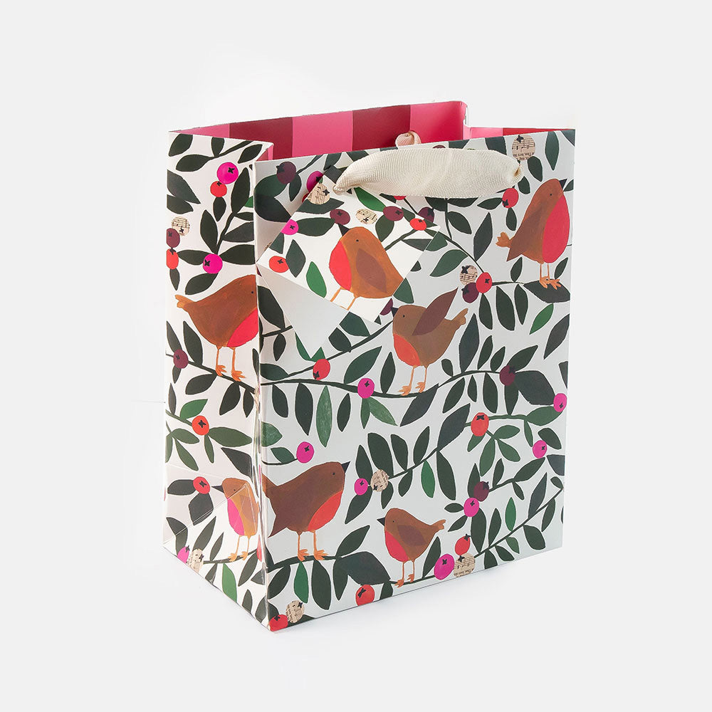 A square gift bag with a white base printed with a pattern of robins, leaves, and berries, featuring pink and red striped inner lining and cream canvas handles.