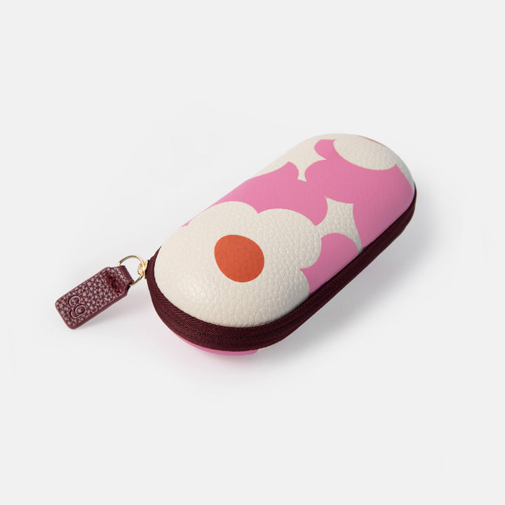 A compact, zippered eyeglasses case with a playful pink and off-white abstract pattern, featuring a small orange circle detail and a dark brown textured zipper pull.