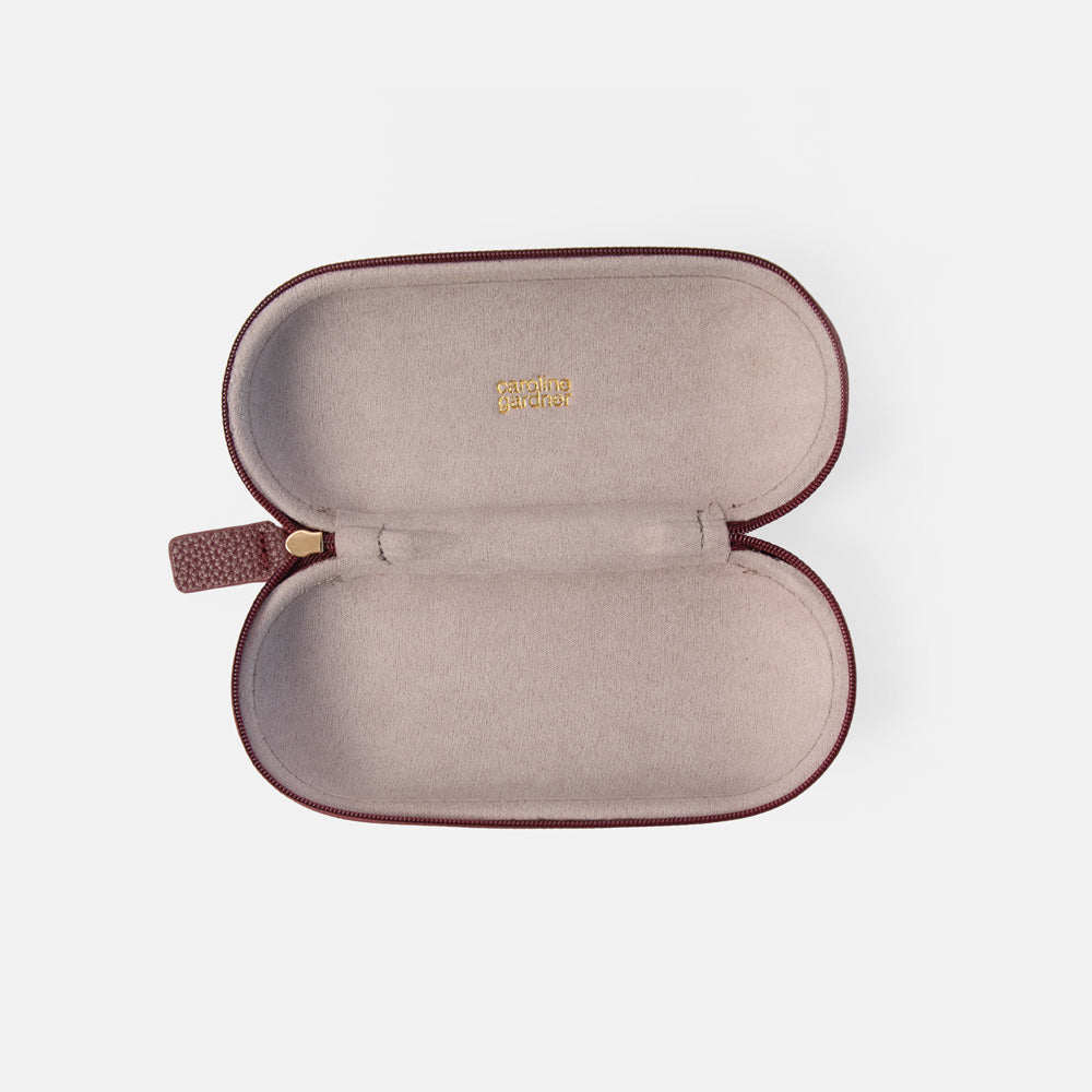 An open eyeglasses case with a dusty rose interior and dark burgundy exterior, featuring a small gold logo on the inside lid and a matching burgundy zipper pull.