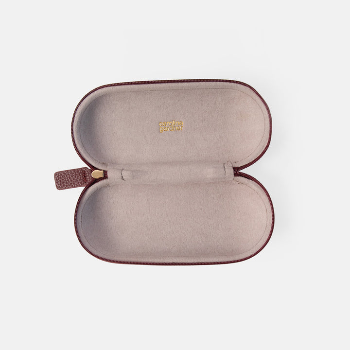 An open eyeglasses case with a dusty rose interior and dark burgundy exterior, featuring a small gold logo on the inside lid and a matching burgundy zipper pull.