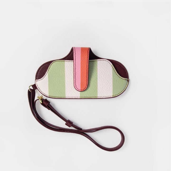 A small pebbled glasses case with a multicolor striped pattern in sage green, white, pink, and coral, featuring dark burgundy leather trim and a matching dark burgundy wrist strap, shown on a light gray background.