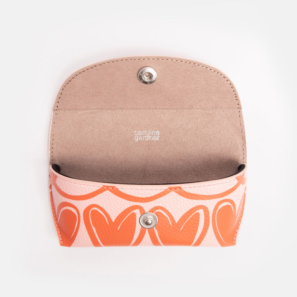 pink flap close glasses case with orange looped hearts design, popper closure, and 'caroline gardner' internal branding
