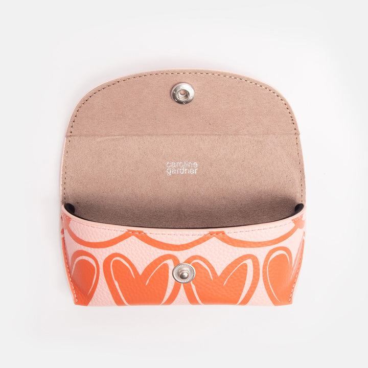 pink flap close glasses case with orange looped hearts design, popper closure, and 'caroline gardner' internal branding