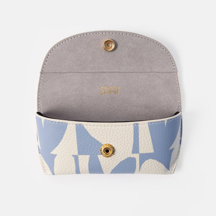 blue heart print glasses case, open to show the lining. The exterior has a light blue and off-white geometric pattern with pebbled texture, and the interior is a smooth light gray suede-like material with gold-tone hardware and the brand name 'Caroline Gardner' printed inside.