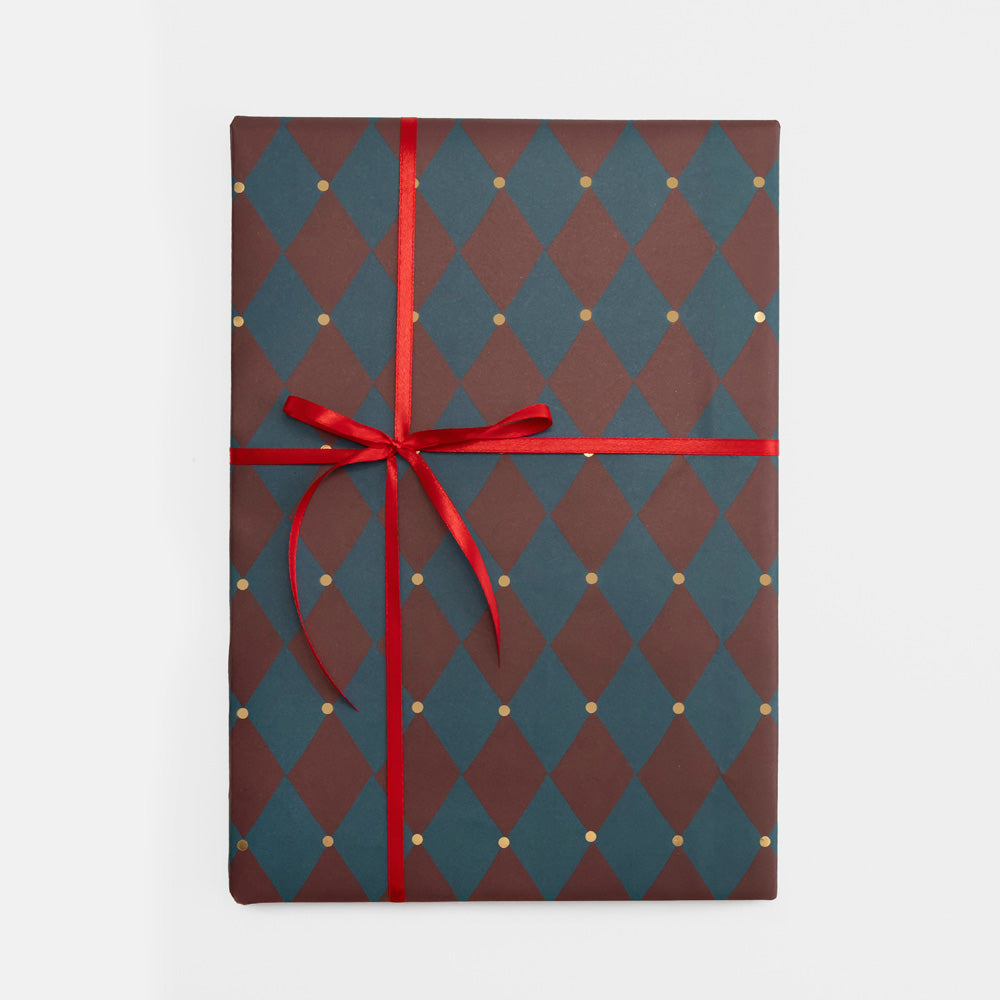 A gift wrapped in a burgundy and teal harlequin diamond patterned paper with small gold dots, tied with a red ribbon and bow, on a light gray background.