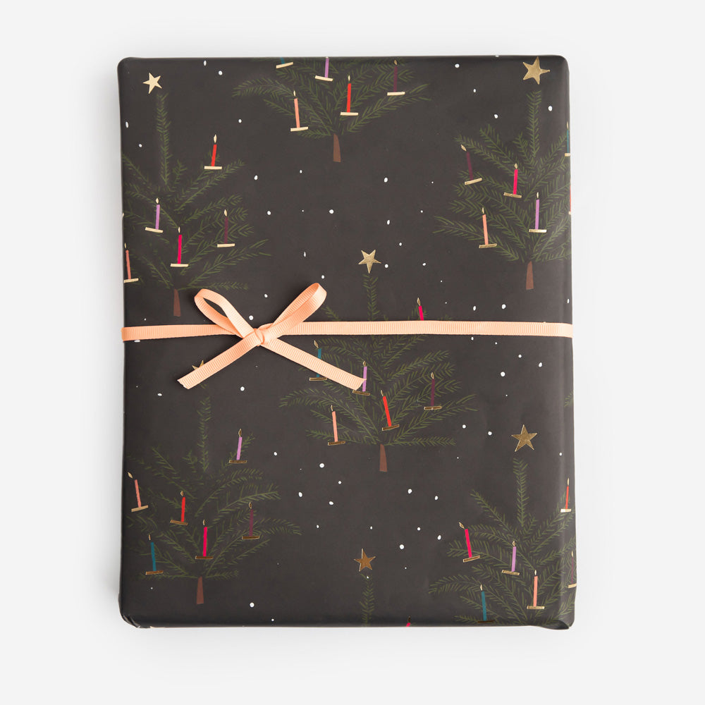 Gift wrap with Christmas tree and candle pattern on a dark background, tied with a beige ribbon.