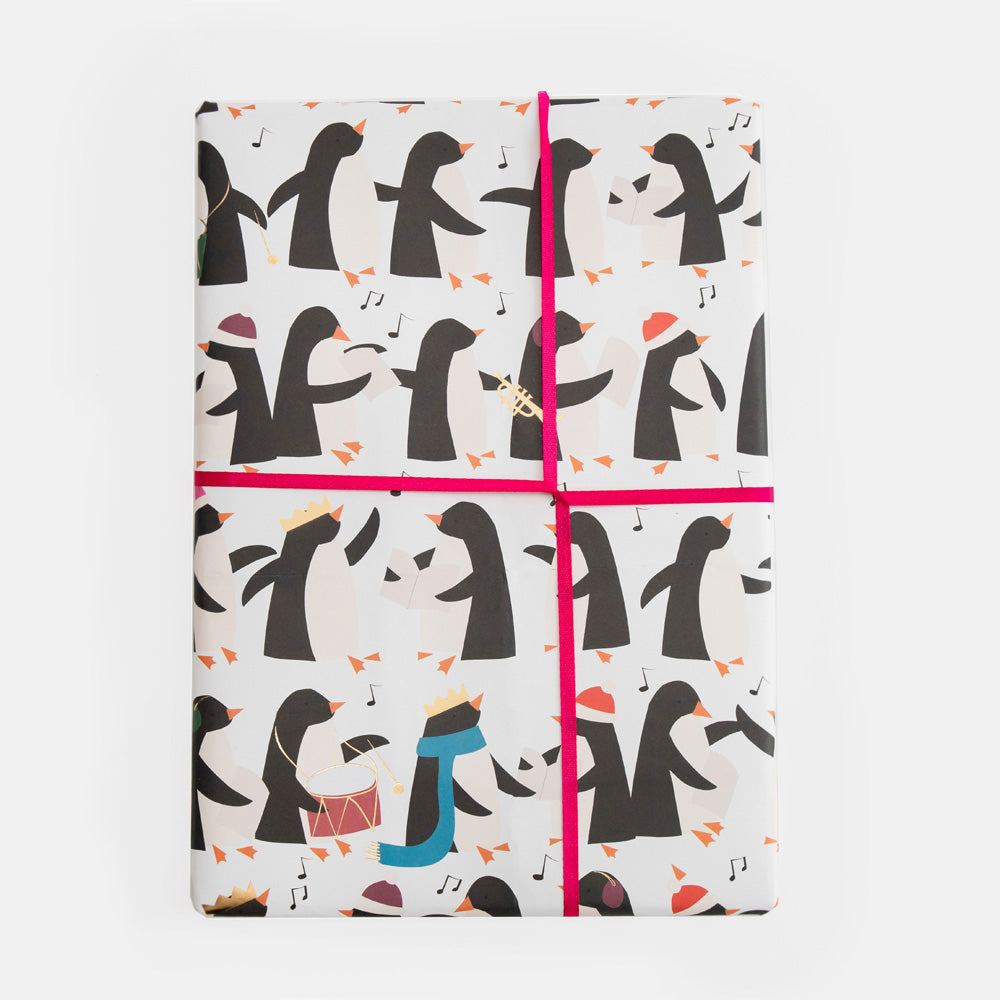 Christmas wrapping paper with a black and orange penguin pattern, tied with a bright pink ribbon in a cross shape.