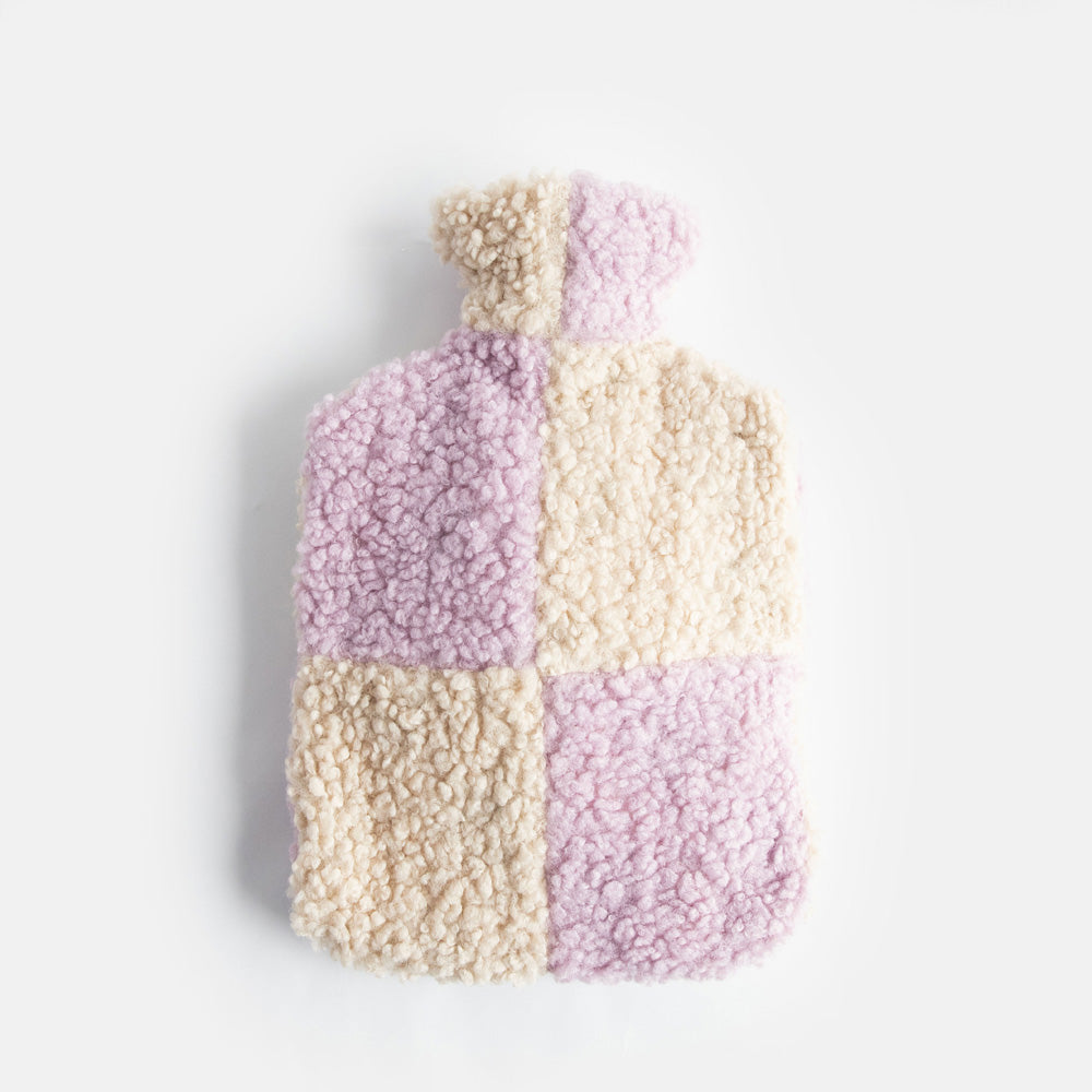 hot water bottle with a synthetic borg cover in a lilac and cream check design and a zipped closure