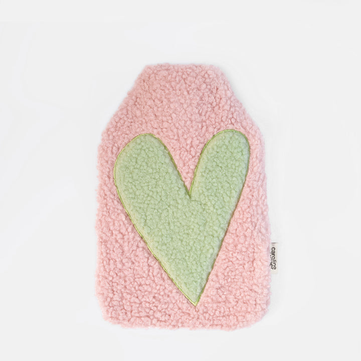 A pink fuzzy sheepskin hot water bottle with a large light green heart applique in the center, shown on a plain white background.