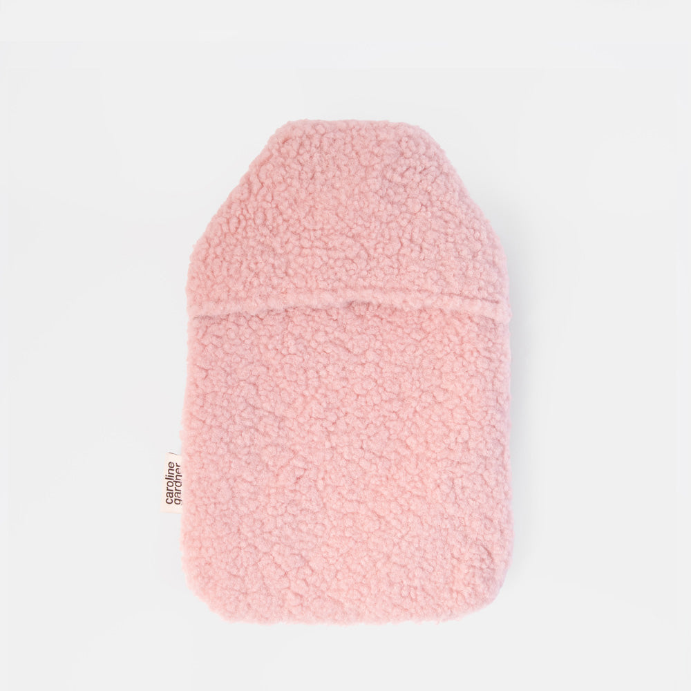 A light pink borg hot water bottle, shown flat against a solid white background. A small vertical tag on the left side reads 'caroline gardner'.