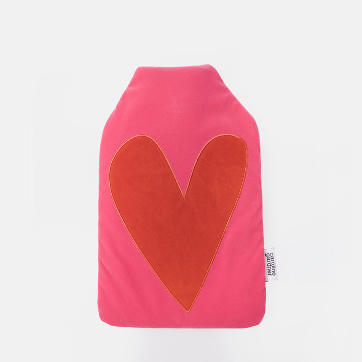 A hot water bottle in bright pink fabric with a large orange-red heart applique on the front, shown against a plain white background.