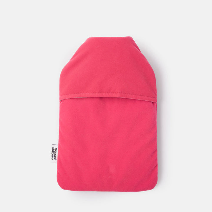 A bright pink fabric pouch or sleeve with a curved top and a horizontal seam across the middle, shown flat against a light gray background. A small black-and-white tag is visible on the left edge.
