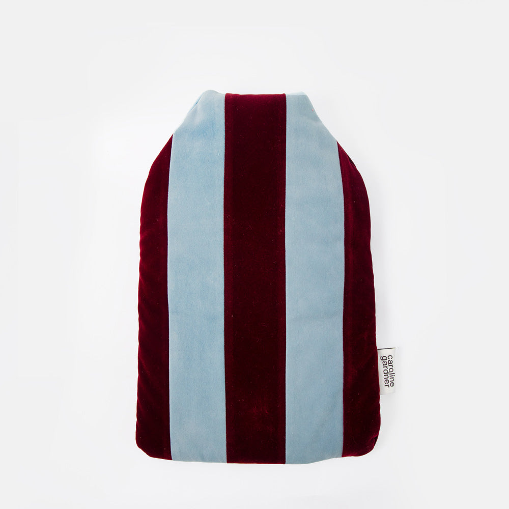 A plush velvet hot water bottle with vertical stripes in burgundy and light blue, featuring a small white sewn-in tag on the right side.