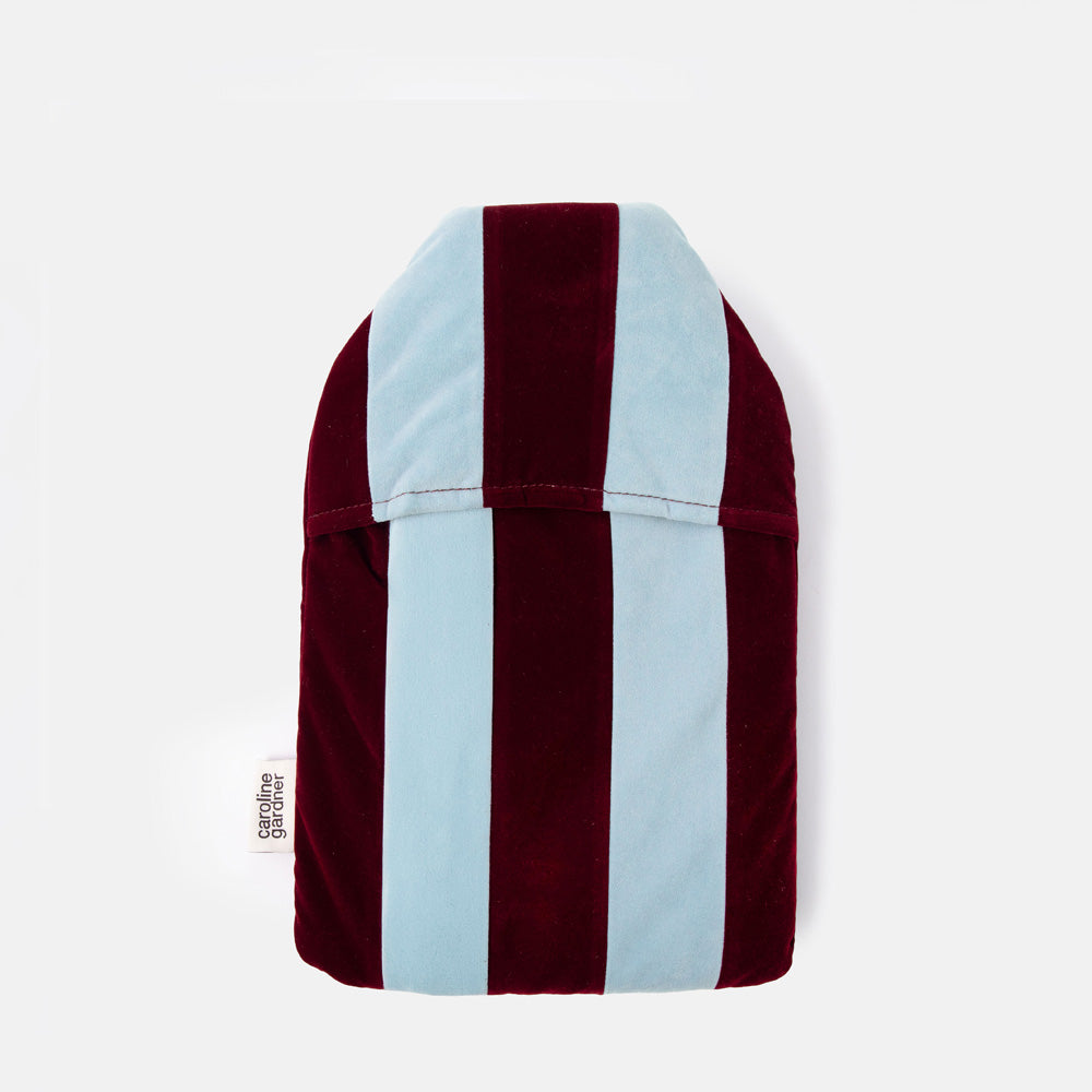 A plush velvet hot water bottle with vertical stripes in burgundy and light blue, featuring a small white sewn-in tag on the right side.