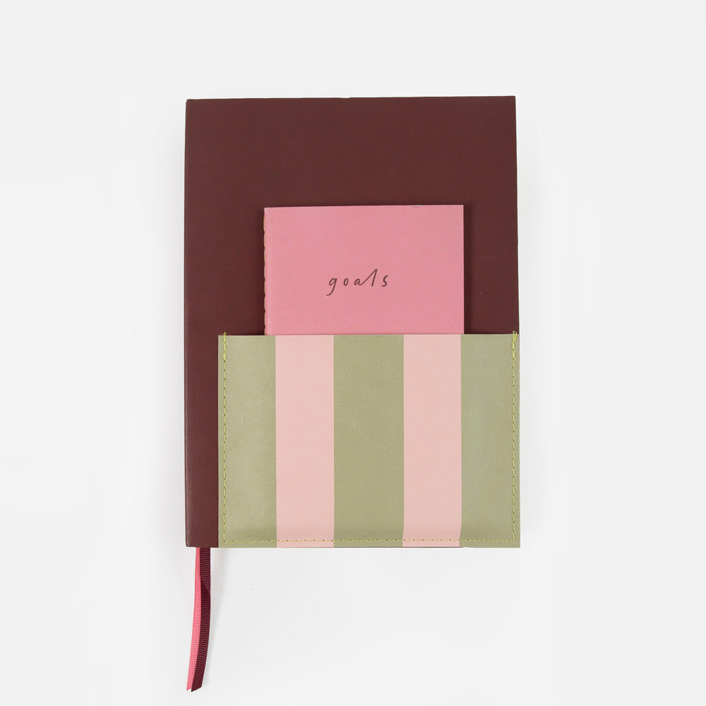 A structured notebook or planner with a dark brown cover, a pink pocket page labeled 'goals', and a striped pocket in shades of sage green, light pink, and peach, shown on a clean white background.