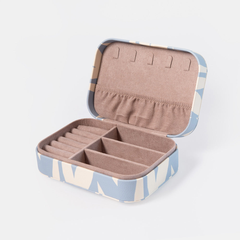 An open rectangular jewelry organizer box with a light blue and cream geometric patterned exterior and a soft blush-beige interior. The box is divided into multiple compartments and features ring loops on the inside lid, photographed on a clean white background.