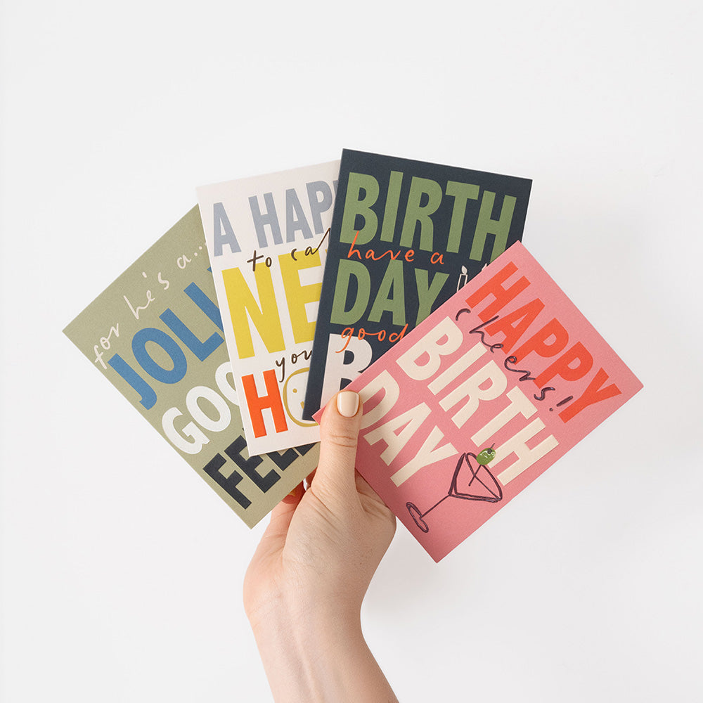 A hand holds four colorful birthday greeting cards fanned out against a clean white background.