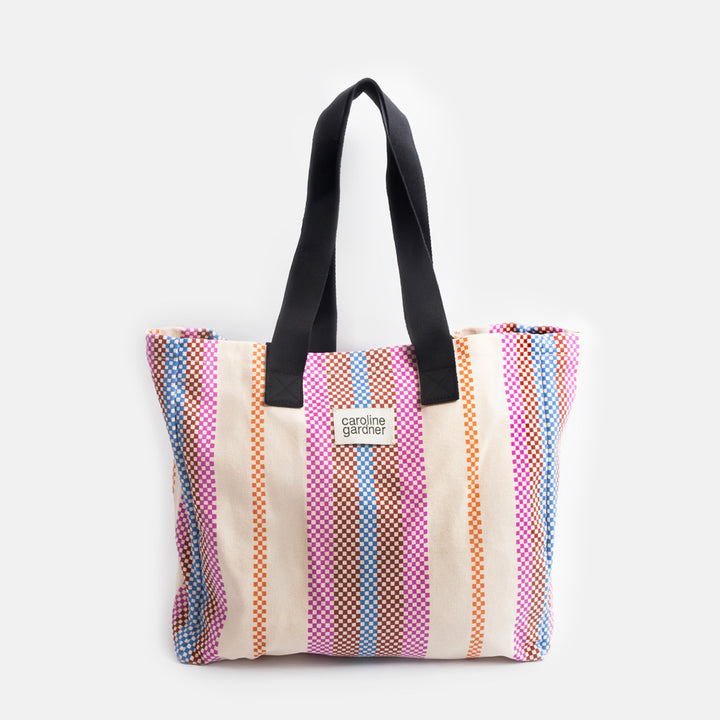 multi coloured checkerboard stripe large tote bag with black handles and 'caoline gardner' branded tab