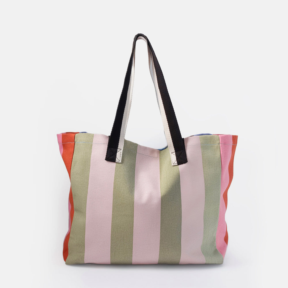 A striped canvas tote bag with vertical stripes in pink, sage green, and orange, featuring black shoulder straps with silver metal hardware, set against a plain white background.
