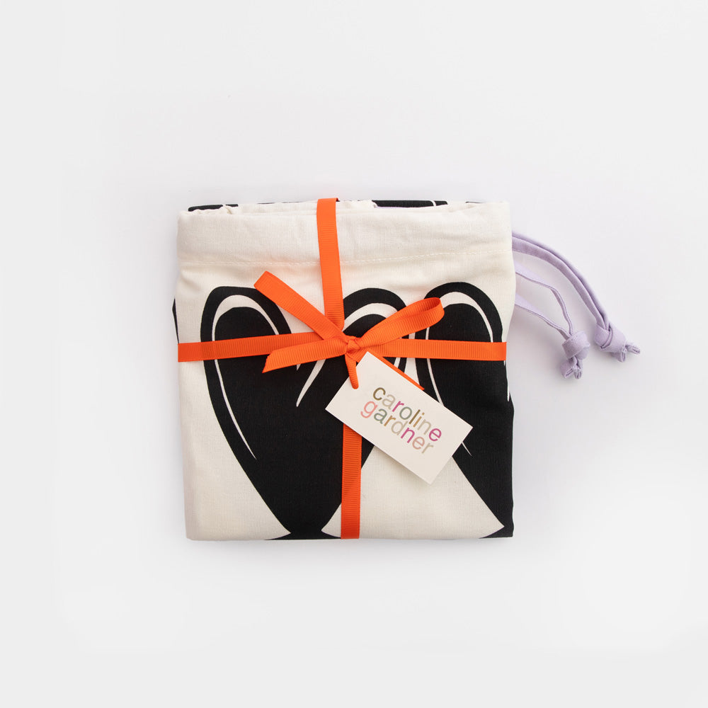 Drawstring laundry bag with black heart pattern on a white background packaged with orange ribbon and 'caroline gardner' branded tag