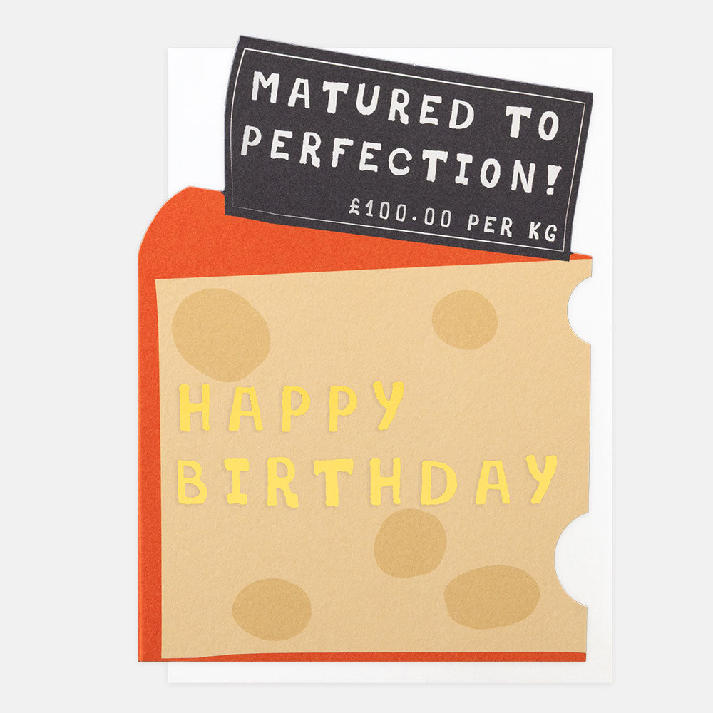 A novelty birthday card designed to look like a slice of cheese with orange rind, tan face, and yellow 'HAPPY BIRTHDAY' lettering. A black label at the top reads 'MATURED TO PERFECTION! 