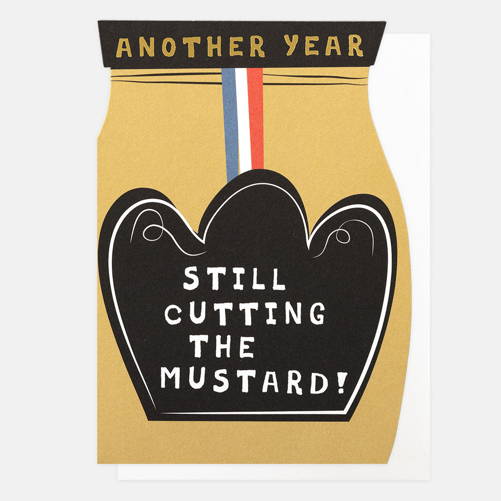 A novelty greeting card featuring a mustard-yellow jar silhouette with a black heart-shaped label that reads 'STILL CUTTING THE MUSTARD!' and a top banner reading 'ANOTHER YEAR' in gold text.