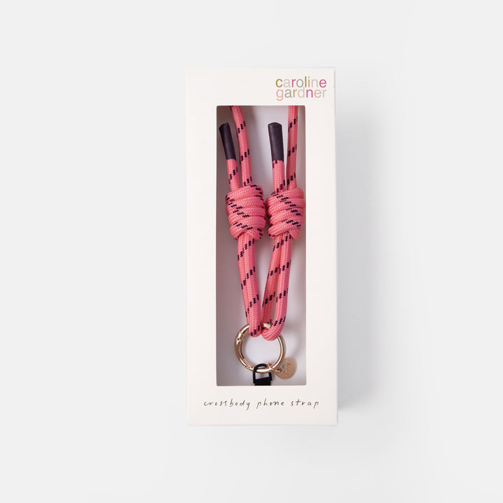 Caroline Garder Phone Strap in pink and black patterned cord with a gold-tone ring, shown in its white retail packaging box against a light gray background.
