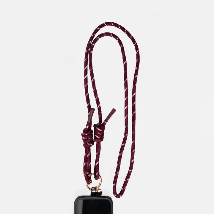 A burgundy and white patterned braided rope lanyard phone strap with a knotted loop and a gold metal ring, shown hanging from a black phone case against a light gray background.