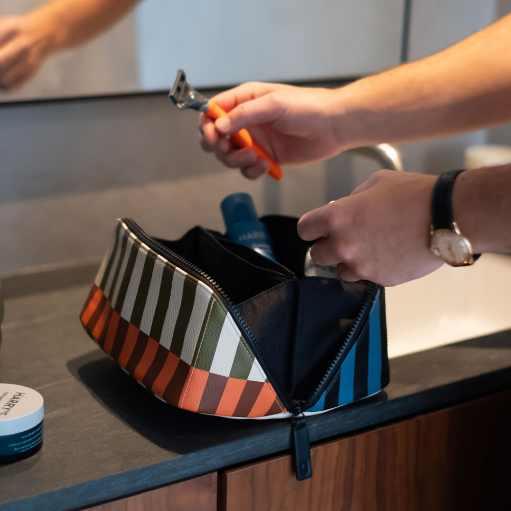 diagonal zip flat lay vegan leather wash bag in retro stripe print in orange, brown, green, white and blue