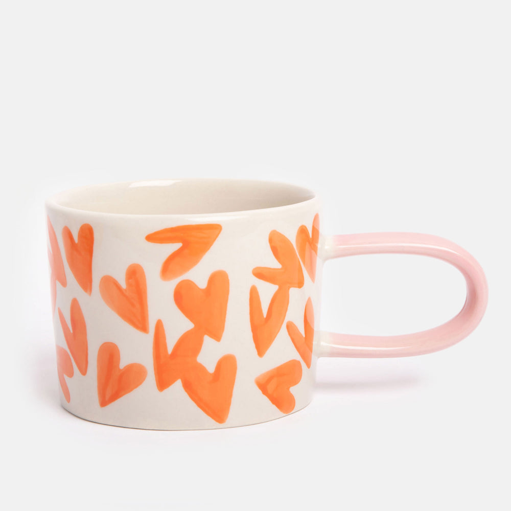 hand painted ceramic stoneware mug with bright orange hearts design and pale pink elongated handle