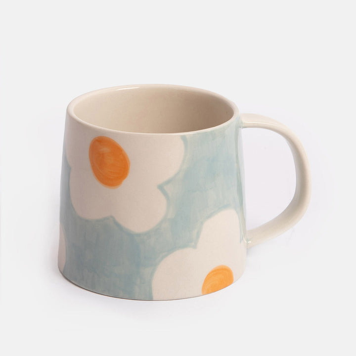 light blue mug with white and orange flower design on a light grey background