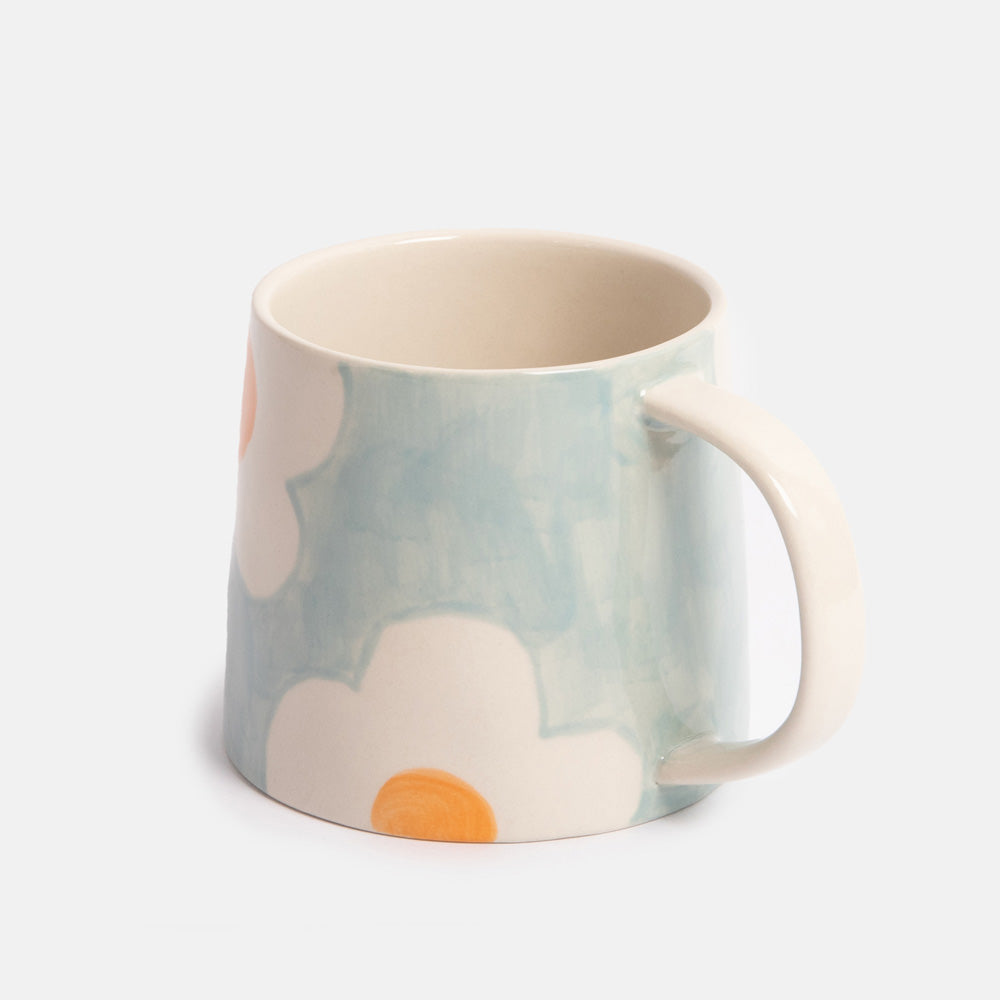 light blue mug with white and orange flower design on a light grey background