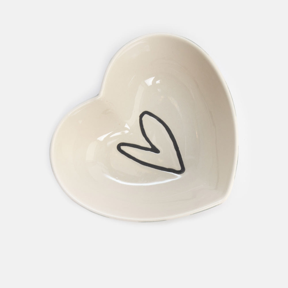 A heart-shaped ceramic dish in a warm cream color, featuring a simple black hand-drawn heart outline in the center, set against a clean white background.