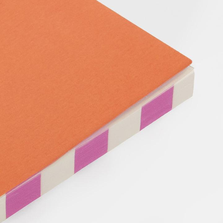 Close-up of a notebook with an orange cover and pink stripes on a white background
