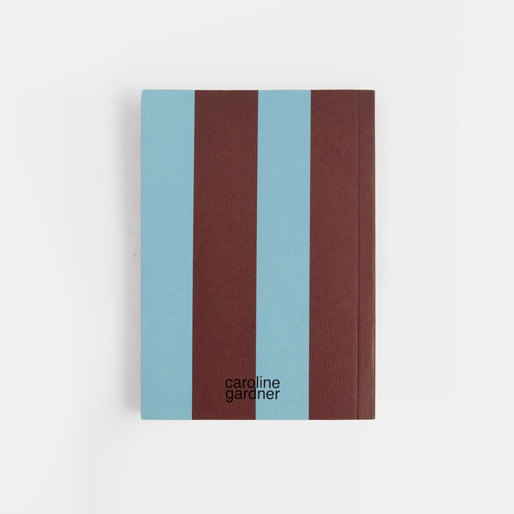 A hardcover notebook by Caroline Gardner with three vertical stripes in light blue, dark brown, and light blue, shown on a clean white background.