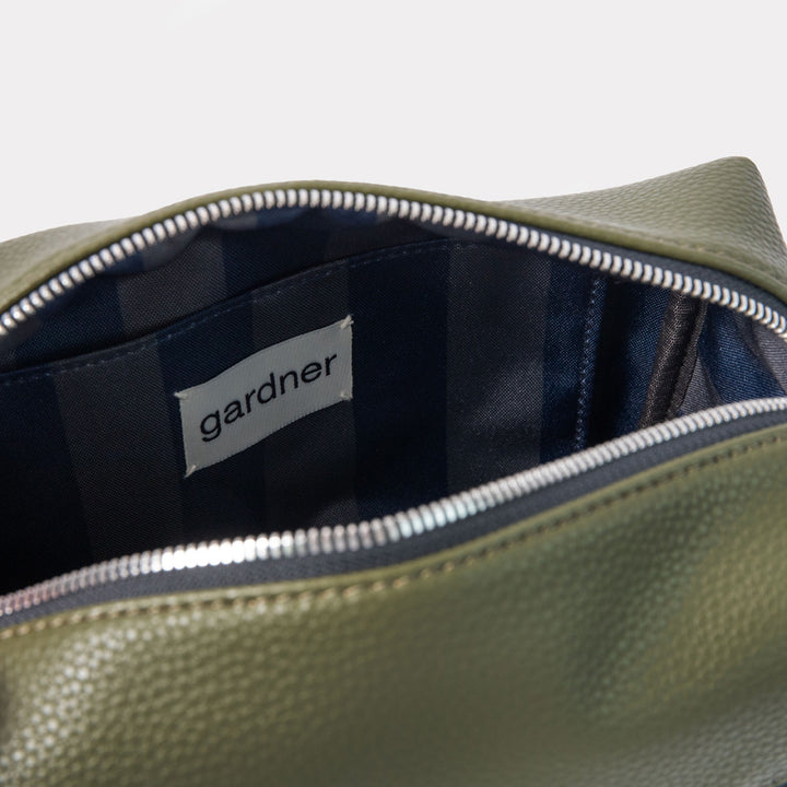 khaki green leather look wash bag with silver zipped main compartment featuring blue and green internal lining and 'gardner' branded tab