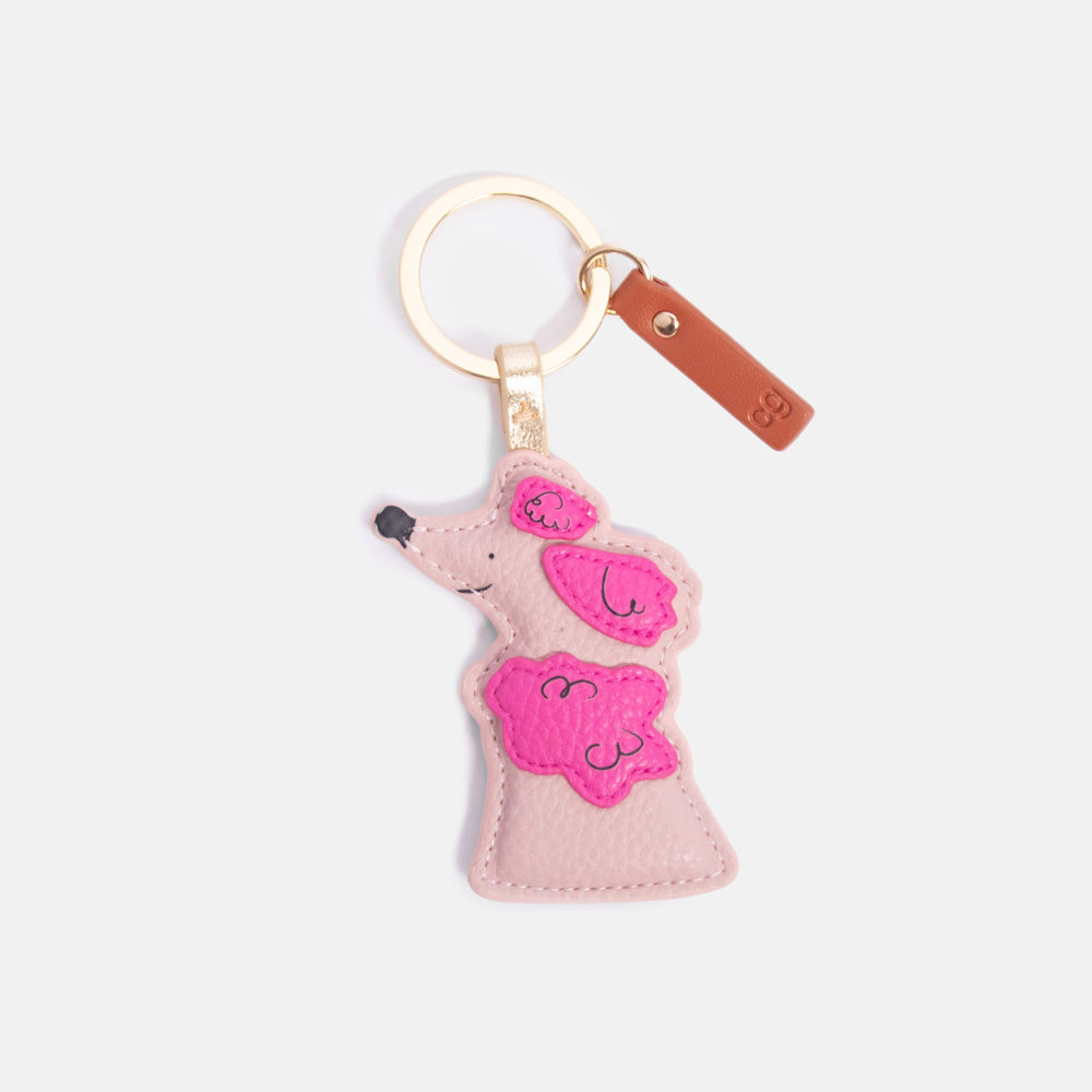 Pink poodle-shaped keyring with a brown tab on a light grey background