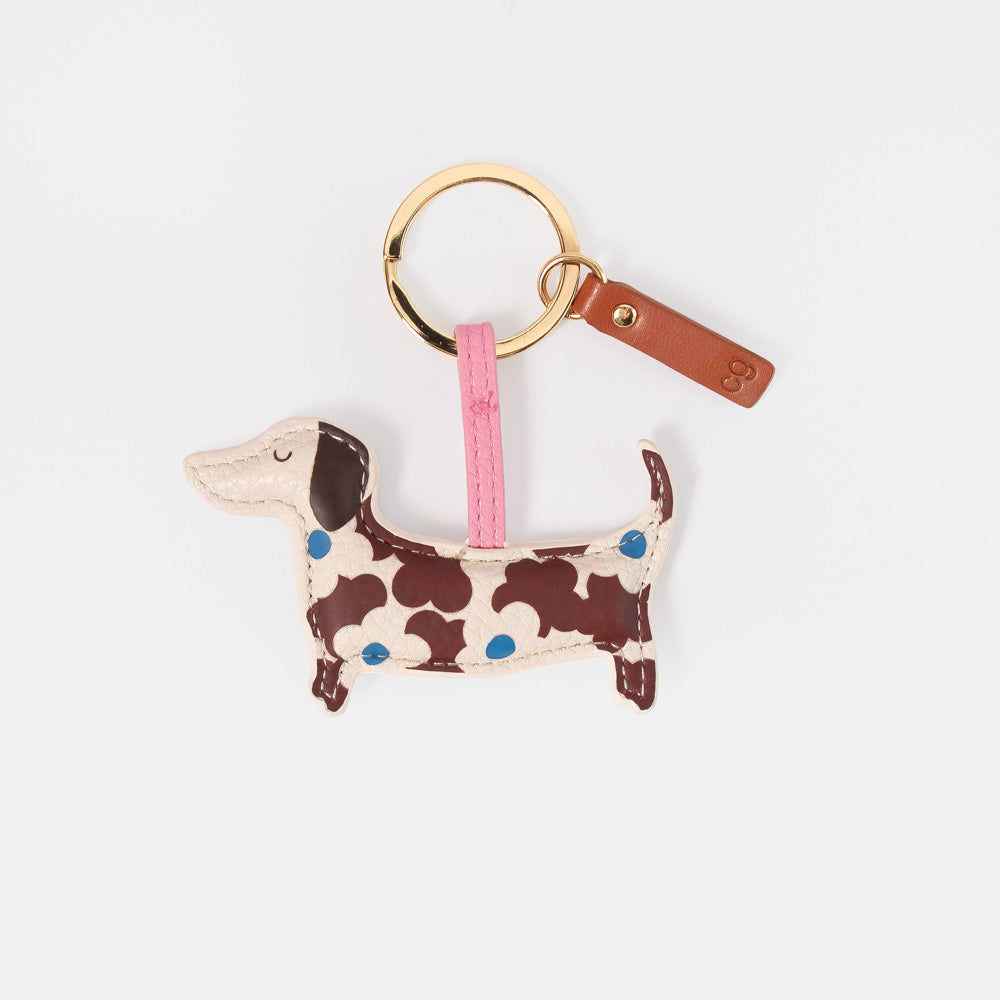 A dachshund-shaped keyring in brown & blue floral design, attached to a gold split ring and a brown leather tag on a light gray background.
