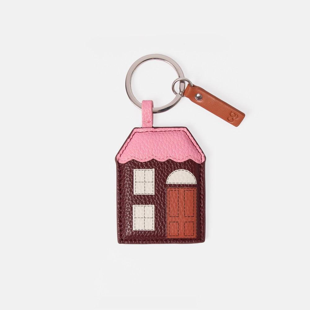 A small house-shaped keyring charm in pink and brown faux leather with a silver metal key ring and a brown leather tag, shown on a light gray background.