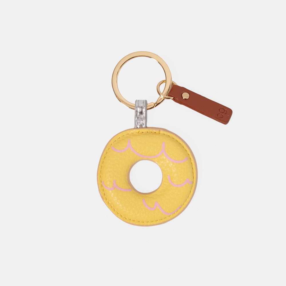 A yellow faux-leather party ring biscuit keyring with pink icing details, a gold-tone split ring, and a brown leather tag on a light gray background.