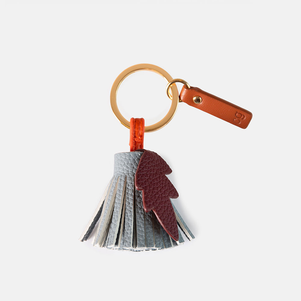 A leather tassel keyring featuring a split design with light gray and dark burgundy textured leather strips, attached to a gold-tone split ring and a brown leather tag.