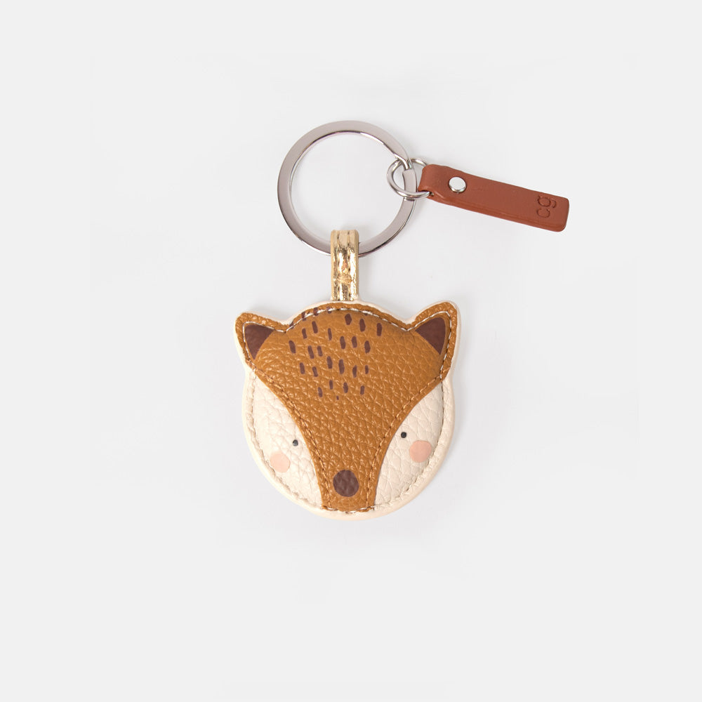 A small fox head keyring or bag charm made of textured faux leather in brown and cream, attached to a silver metal key ring with a brown leather tag on a light gray background.