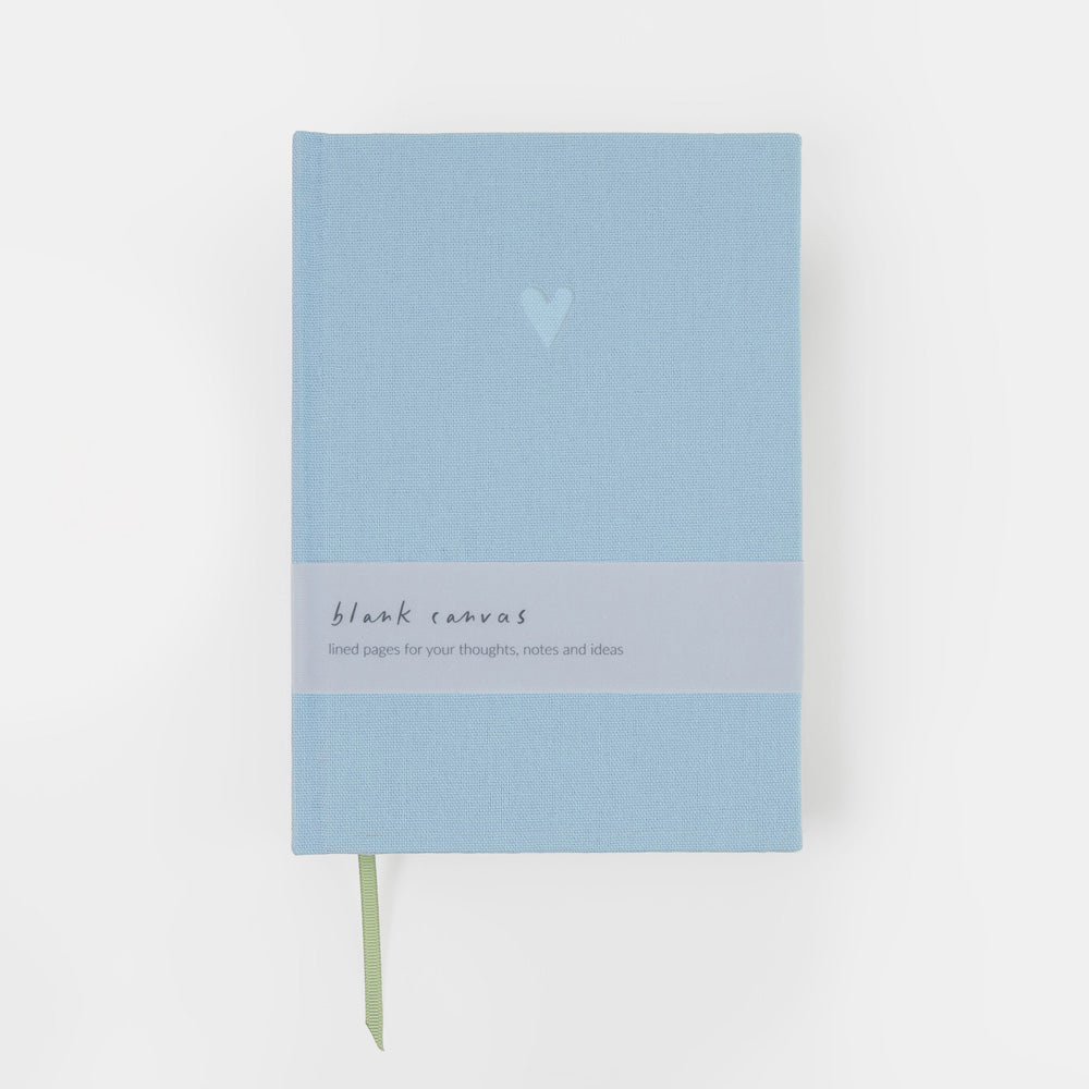 A light blue hardcover notebook with a white band around the middle reading 'blank canvas' and a small heart printed near the top, shown on a clean white background.